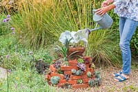 Woman using watering can to water finished succulent tower