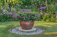 Focal point pot on circular base set into lawn, colour themed borders behind