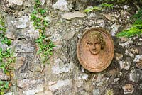 Terracotta roudel of a woman's head on a stone wall with ivy 