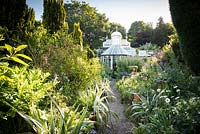 Rare Mackenzie and Moncur glasshouse surrounded by lush planting including silvery astelias in the walled garden at Glassmount