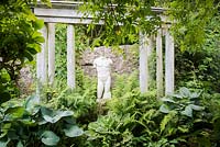 Classical statue framed by temple columns and lush planting including ferns and hostas in June