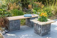 Gabion and scaffolding board bench and table on slate patio in modern garden. 