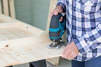 Using a cordless jigsaw to cut roof shape in shed back panel