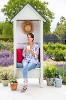 Woman enjoying a hot drink whilst sitting in a shed covered seat furnished with cushions