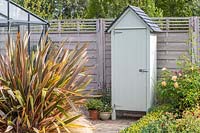 Mini garden shed fitted with a door on path next to wooden fence
