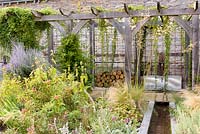 Courtyard garden with timber pergola, rill, galvanised trough water feature and planting including Stipa tenuissima, S. gigantea, Phlomis russeliana, Perovskia 'Blue Spire', irises and silvery stachys at Am Brook Meadow, Devon in August. 