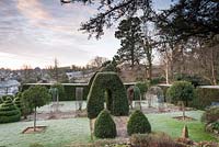 Formal garden with clipped bay, box, standard Portugese laurels and rose arches over a cobbled path at the Old Rectory, Netherbury, UK. 