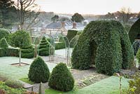 Formal garden with clipped bay, box, standard Portugese laurels and rose arches over a cobbled path at the Old Rectory, Netherbury, UK.