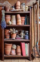 Wooden shelves in a garden shed full of pots, tools, jars, seeds and books