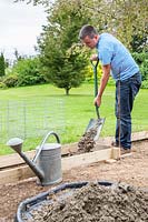 Man shoveling concrete mix into wooden frame to create the base for the gabions