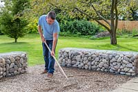 Man using a rake to distribute the pebbles evenly to form a useable surface