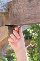 Man adding a screwed eye hook into predrilled hole in timber