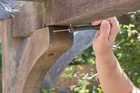 Man using a small screwdriver to twist a screwed eye hook into predrilled hole in timber 