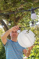 Man fixing white paper lantern over the bulbs in the light chain