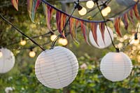 Detail of colourful bunting and lit chains of lights hanging from underside of wooden pergola