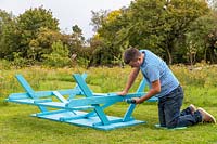 Man assembling a picnic bench - fixing cross bar diagonally to stabilise the structure