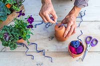 Woman threading purple string through small terracotta pot for hanging 