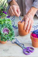 Woman threading purple string through small terracotta pot for hanging