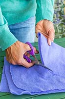 Woman using scissors to cut purple material for lining a hanging basket