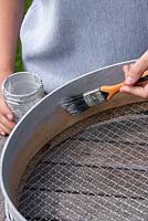 Woman painting wooden sieve with outdoor paint.  Planting Succulent Sieve.  Step 1.