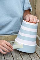 Remove the masking tape covering the first colour coat, revealing a stripey coloured pot.
