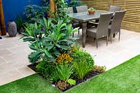 Small patio with dining area, central bed recently-planted includes Edgeworthia chrysantha 'Grandiflora' and Rudbeckia 'Little Goldstar'