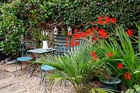 Table and chairs in gravel garden with Crocosmia 'Lucifer'