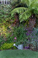 Small garden at night with lights in border with tree fern, Verbena bonariensis, Erysimum 'Bowles Mauve' and Hosta 'Big Daddy'