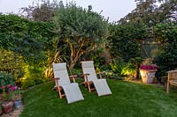 Small garden at night with lights in borders, view across artificial lawn with sun loungers