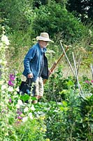 Man wearing sun hat, walking to his plot carrying tools and a bag for harvesting 