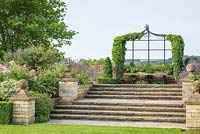 Steps leading up from the lawn to a raised walk with ivy covered arbours at Bourton House
