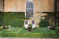 Fountain Garden at Bourton House shaped with box hedges planted with heliotrope and Cyperus alternifolius, clipped ozmanthus and espaliered pyracantha.
