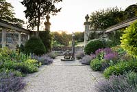 Double border at sunset with pools of Nepeta - Catmint - spilling on to wide path, beyond a framework of architectural fragments 