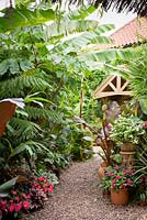 A gravel path framed by plants including impatiens, begonias, Tradescantia 'Blushing Bride', Musa basjoo, Tetrapanax papyrifer 'Rex' and Ensete ventricosum 'Maurelii' leading to the front door of Oak Barn.