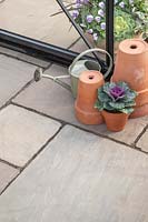 Terracotta pots and metal watering can displayed on mixed size sandstone patio. 