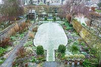 Walled town garden with snow, showing layout with lawn, beds and pleached trees beyond