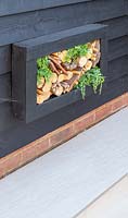 Wall mounted insect hotel with logs, bamboo sticks and tiles. 