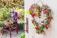 Woven heart-shaped wreath with berries and foliage, hanging on open wooden door, garden beyond 