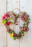 Woven heart-shaped wreath with red berries and foliage hanging on wooden door