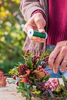 Woman using floristry wire to attach bundles of foliage and berries to a wreath 