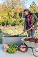 Woman adding compost to container from wheelbarrow using a spade 