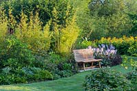 A wooden bench on the edge of one of the island borders with Hosta Halcyon, Bamboo and Phyllostachys aurea. Inula magnifica in the background, Hypericum calycinum in the foreground.