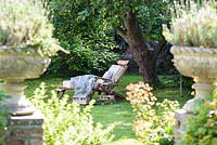 Wooden deckchair lounger with cushions and blanket on lawn in the shade under a tree 