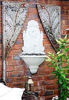 Wall-mounted water feature framed with mosaic panels on brick wall