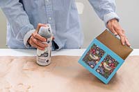 Woman applying spray based clear sealer to the exterior of cardboard box
