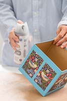 Woman applying spray based clear sealer to the exterior of cardboard box