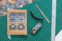 Making wrapping paper decorations on book on work bench with cutting mat, metal rule and craft knife