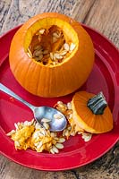 Hollowed out pumpkin on red plate with spoon, pulp and seeds