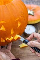 Woman carving halloween face into pumpkin with sharp kitchen knife