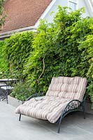 Wide decorative sunlounger with cushion, backed by Wisteria